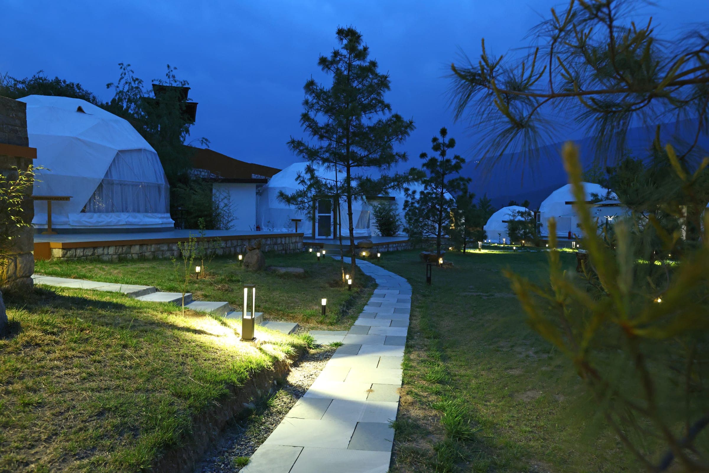 Riverfront glamping domes lit at blue hour along a stone pathway in Paro, Bhutan